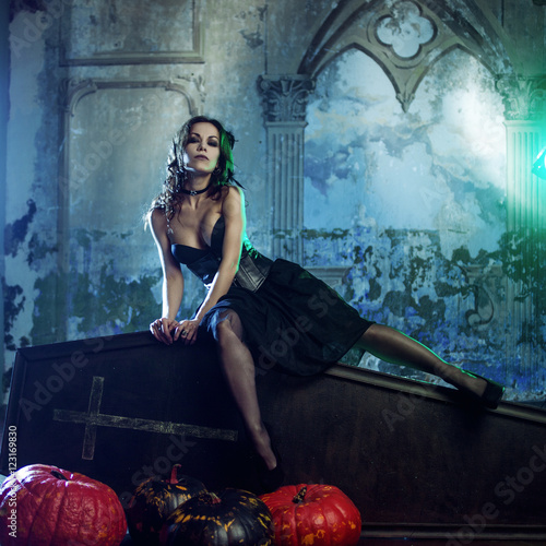 Young and sexy woman  image of witches in a cemetery sitting on lid coffin.