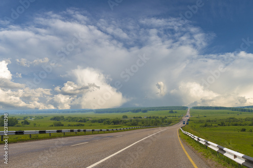 Summer day landscape with clouds, road, field. Countryside landscape.