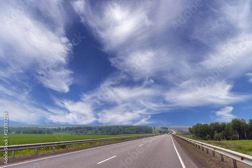 Summer day landscape with clouds, road, field. Countryside landscape.