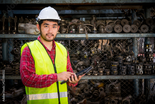 Asian worker with tablet on hands in factory warehouse car parts.