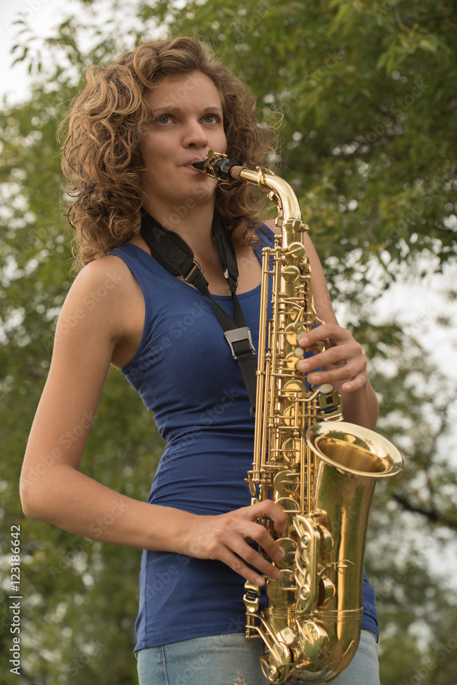 Beautiful girl with curly hair playing the saxophone in gold on Stock
