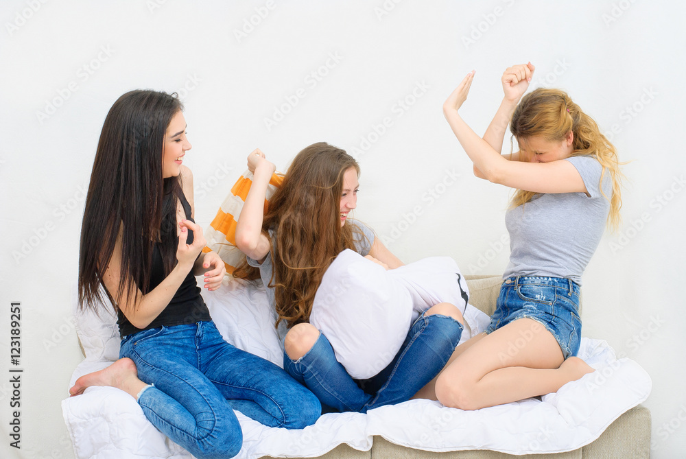 Cheerful beautiful girl friends fighting on the pillows. Active entertainment.