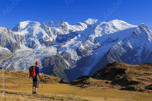 Hiker in a meadow looking towards Mont Blanc, during his hike of the Tour du Mont Blanc. © sanderstock