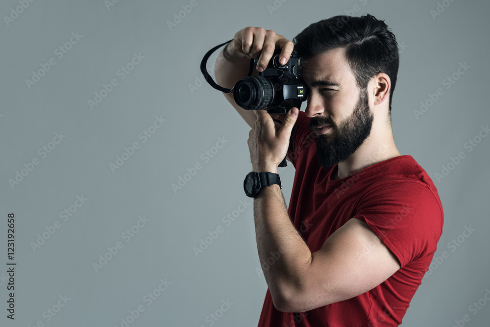 Profile view of young man taking photo with digital single lens camera. Moody desaturated portrait over gray studio background.