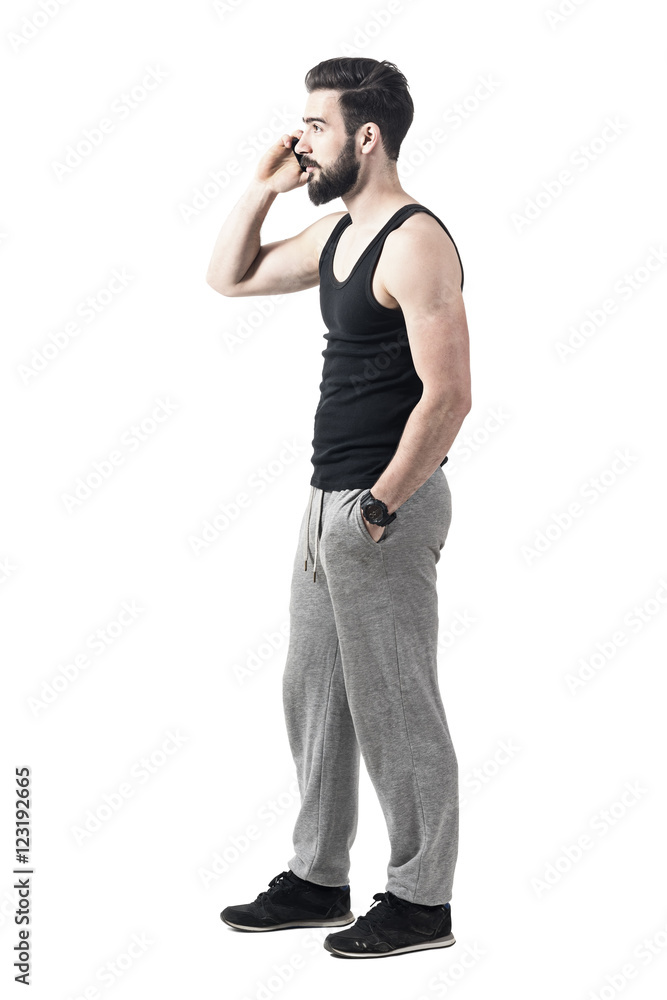 Side view of young fit muscular man on the mobile phone wearing sporty clothes. Full body length portrait isolated over white studio background Side view of young fit muscular man on the mobile phone wearing sporty clothes. Full body length portrait isolated over white studio background