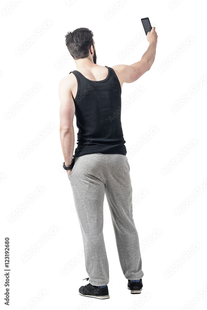 Rear view of muscular gym man taking selfie photo with mobile phone. Full body length portrait isolated over white studio background