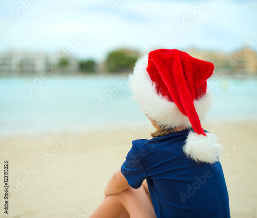 Little girl sitting on the beach. Christmas and new year vacations concept.