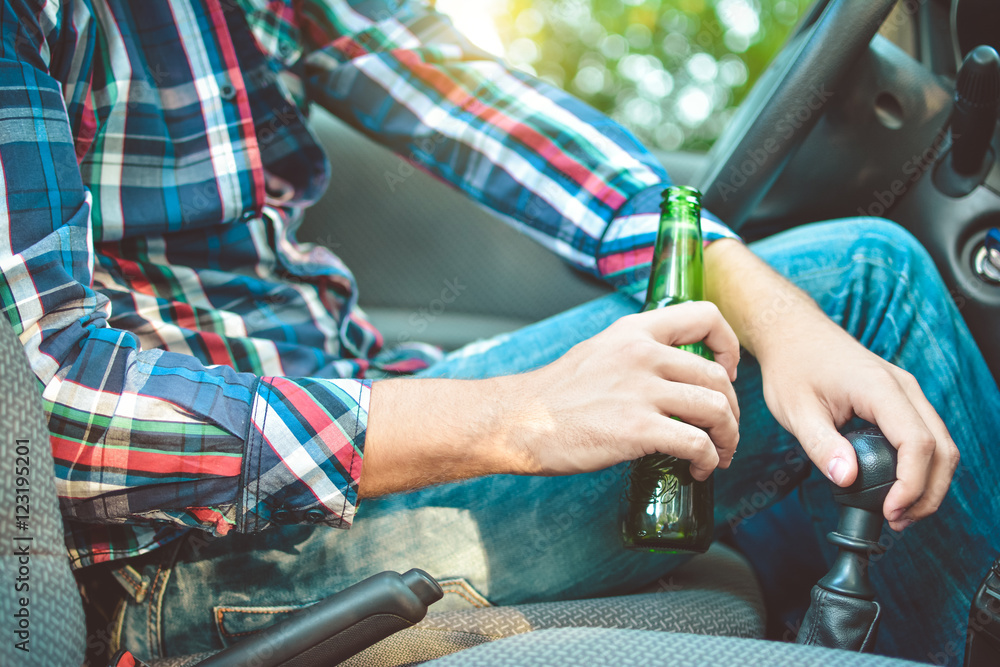 Drunk young man driving a car with a bottle of beer. Don't drink and drive concept. Driving under the influence. DUI, Driving while intoxicated