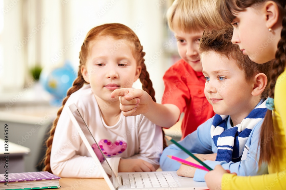 Four schoolchildren sitting at table and looking at laptop screen Four schoolchildren sitting at table and looking at laptop screen