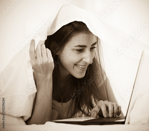 Teenage girl chatting online covered with blanket photo