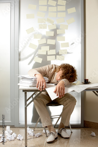 A young man sleeping on table with pile of papers