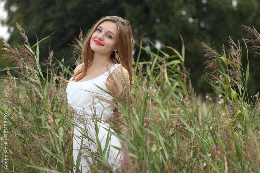 beautiful girl in white dress stand against wild grass