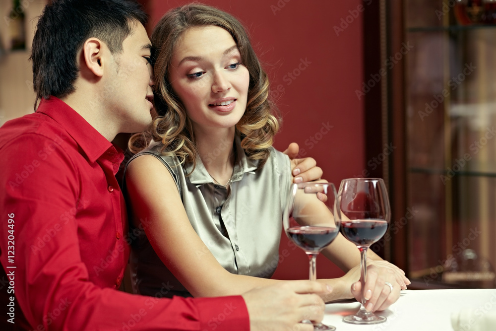 Young man whispering something to his girlfriend ear at restaurant Young man whispering something to his girlfriend ear at restaurant