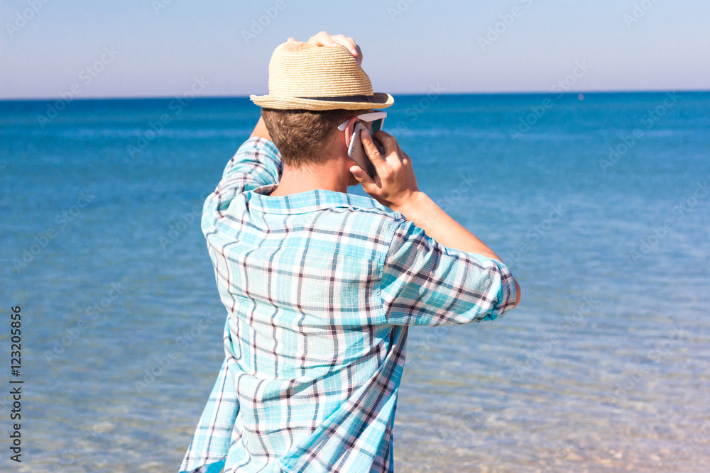 Hipster with hat talking on phone against the sea. Summer holiday