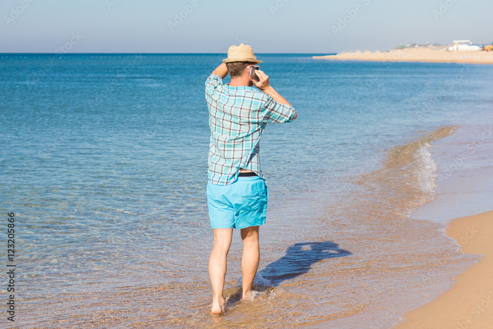 Hipster with hat talking on phone against the sea. Summer holiday