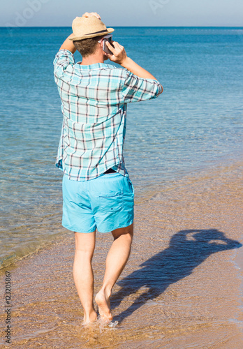 Hipster with hat talking on phone against the sea. Summer holiday