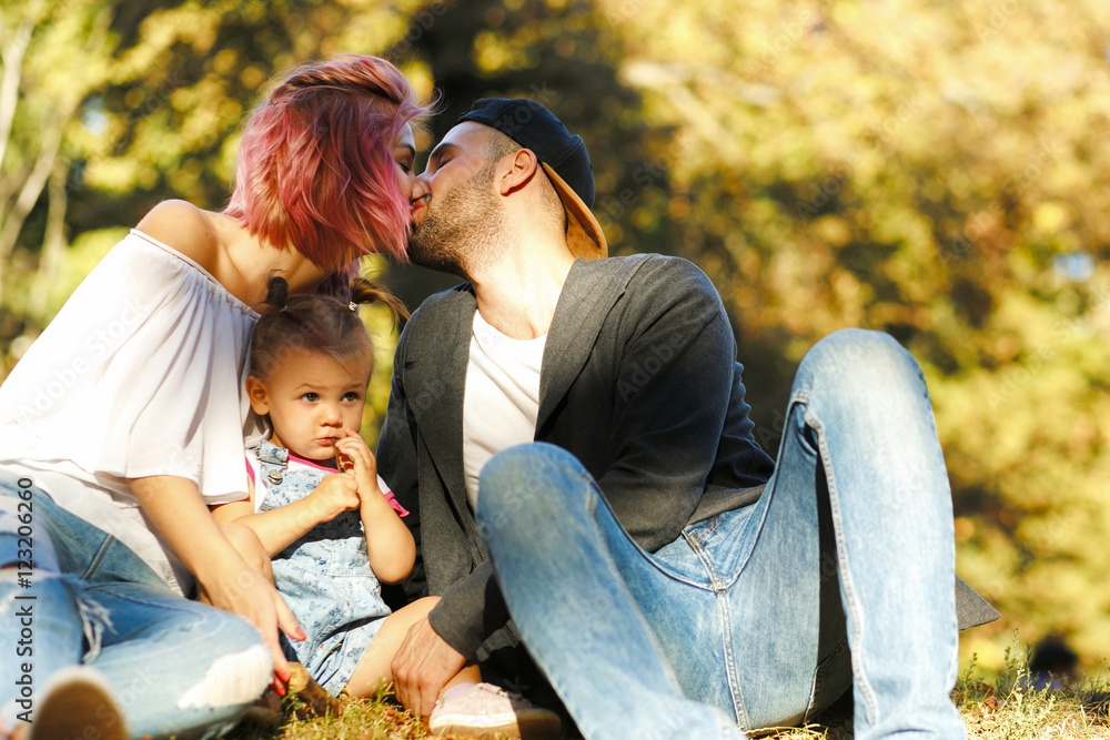 Stylish young parents kiss over their lovely little daughter Stylish young parents kiss over their lovely little daughter