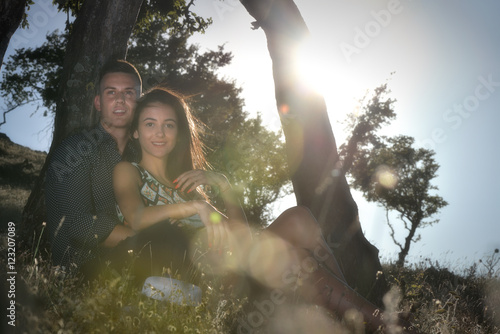 Young couple in love leaning on a tree at sunset with lens flare effect