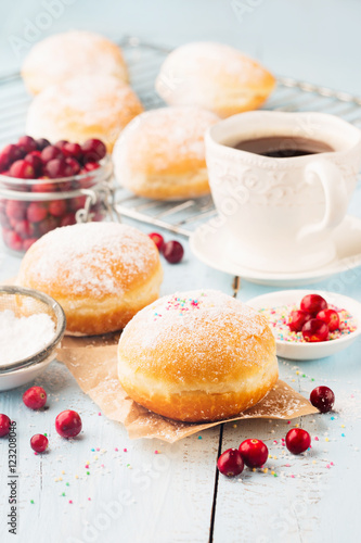 Delicious freshly baked doughnuts with powdered sugar and cup of coffee on blue rustic wooden background.