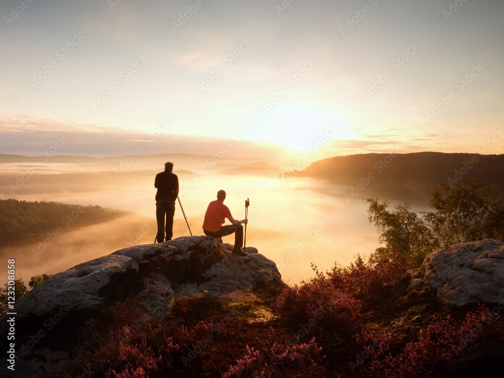 Hiker and photographer with tripod on rock and takes photos. Dreamy fogy landscape,