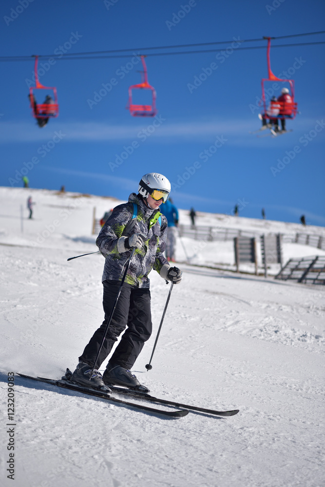Young man skiing downhill with blue sky and chairlift in the background