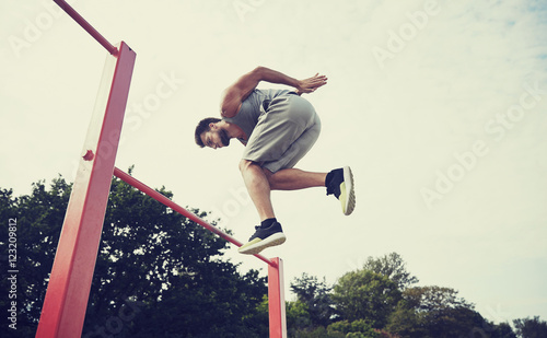 young man jumping on horizontal bar outdoors