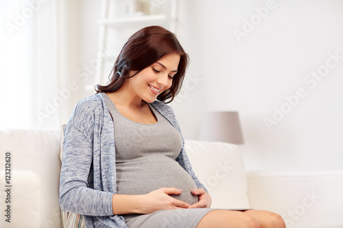 happy pregnant woman sitting on sofa at home