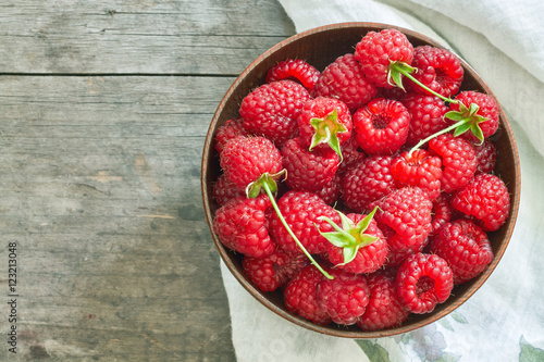 Fresh raspberries in wooden bowl on grey rustic wooden background. Top view with copy space