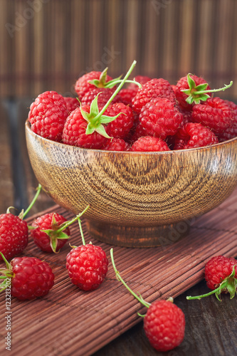 Fresh raspberries in wooden bowl on wooden background. Copy space