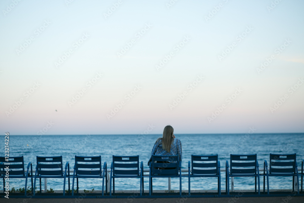 Blonde woman sits on the chair looking at blue city