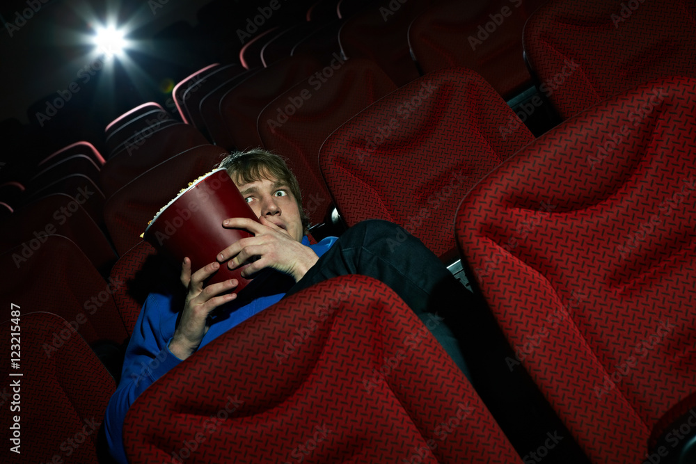 Naklejka premium Young man sitting terrified in cinema hall