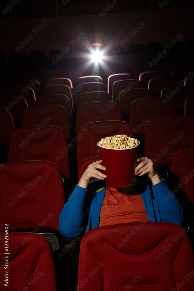 Naklejka premium Young man hiding behind popcorn bucket while watching horror film