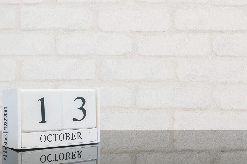 Obraz premium Closeup white wooden calendar with black 13 october word on black glass table and white brick wall textured background with copy space , view another more date in my portfolio