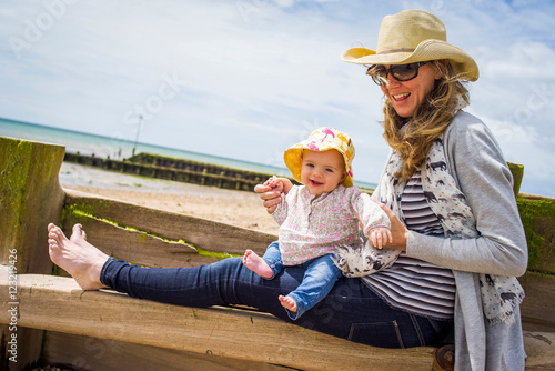 Mid adult woman and baby daughter sitting on beach groyne, Ferring Beach, West Sussex, UK photo