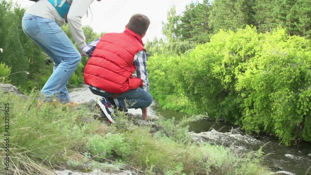 Slow motion of camping father and son sitting on steep rocky shore looking and pointing at fast flowing river Slow motion of camping father and son sitting on steep rocky shore looking and pointing at fast flowing river