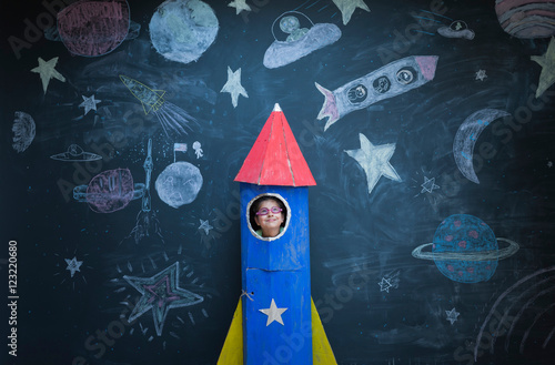 Portrait of girl in handmade space rocket in front of space themed chalk drawings photo