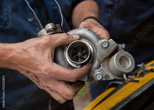 the hands of mechanics hold the turbine of a car motor