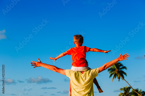 happy father and little son on shoulders play at sky