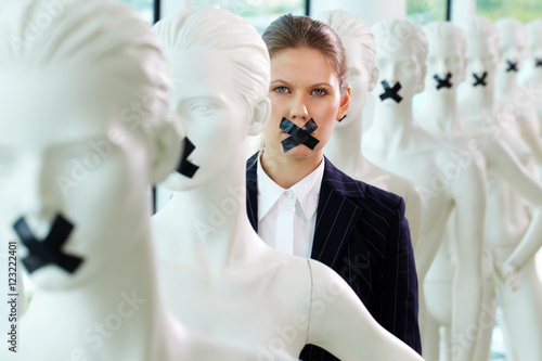 A woman standing in line of mannequins with taped mouth photo