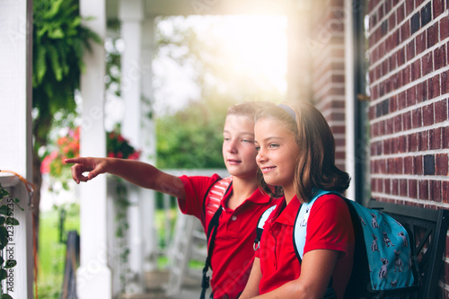 Twin brother and sister sitting on bench pointing, on first day of new school year photo