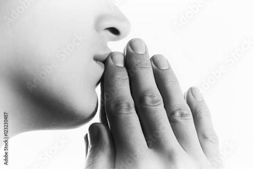 Black and white image of  a  woman  during a prayer on white background. Her hands touchs  a lips.