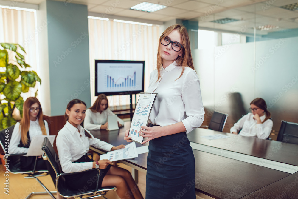 Beautiful business woman in glasses on the team's background with documents in hand