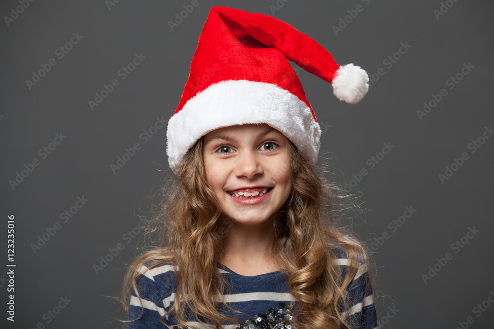 Close up portrait of a smiling little girl in a christmas cap, gray background Close up portrait of a smiling little girl in a christmas cap, gray background