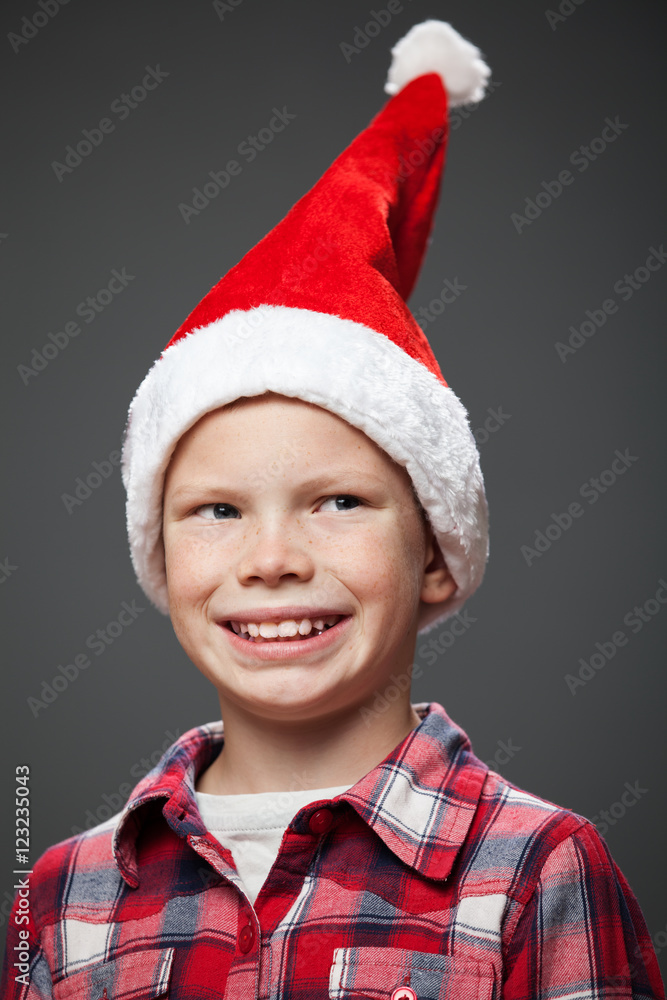 Close up portrait of a smiling little boy in a christmas cap and red shirt, gray background Close up portrait of a smiling little boy in a christmas cap and red shirt, gray background