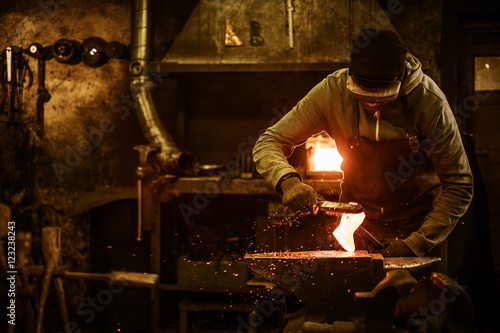 The blacksmith with brush handles the molten metal on the anvil in smithy