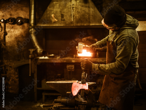 The blacksmith forging the molten metal on the anvil in smithy