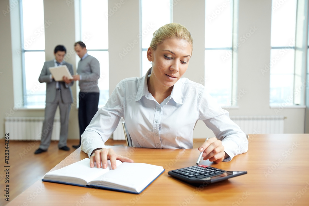 Female accountant working in office with business people in the background Female accountant working in office with business people in the background