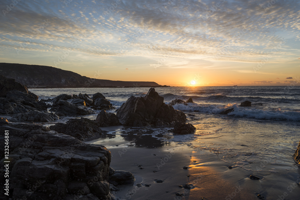 Fototapeta premium Kennack sands beach at sunrise with rocky beach and beautiful cloudy sky, Cornwall, UK