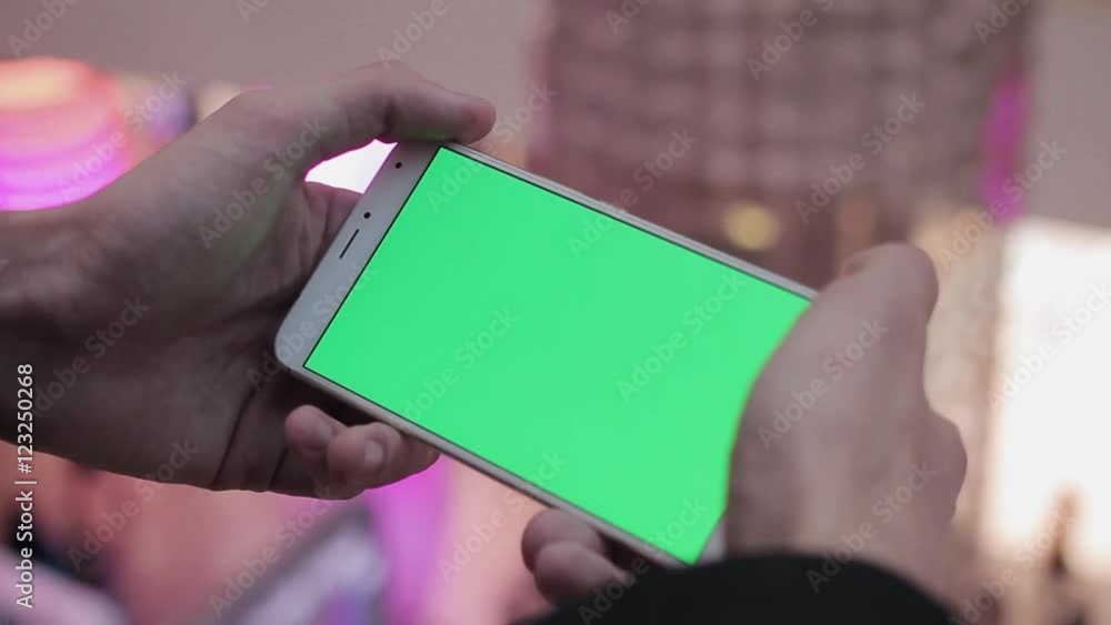Male hands using smartphone with green screen in shopping mall. Lot of people at the background Male hands using smartphone with green screen in shopping mall. Lot of people at the background