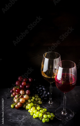 Wine in glasses and different types of grape on dark background.
